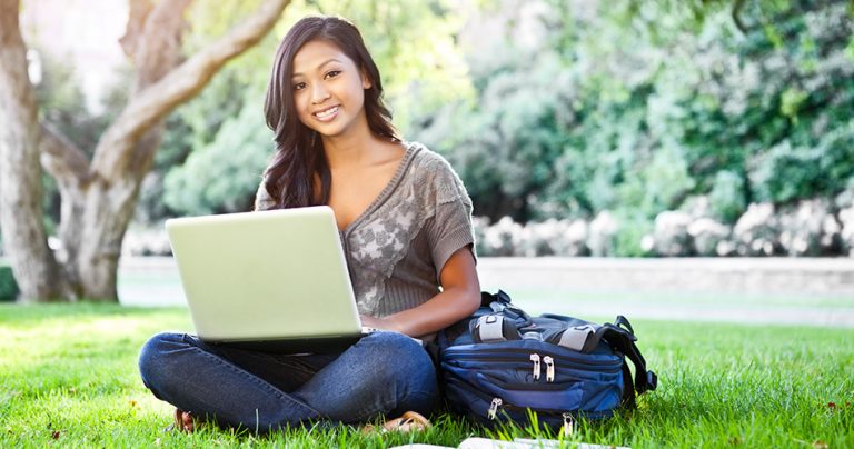 Etudiante souriante dans un parc avec son ordinateur portable