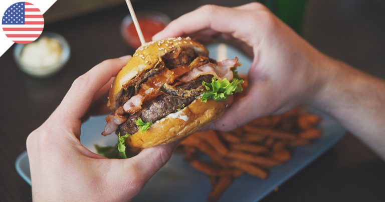 Gros plan sur les mains d'une personne qui mange un énorme hamburger